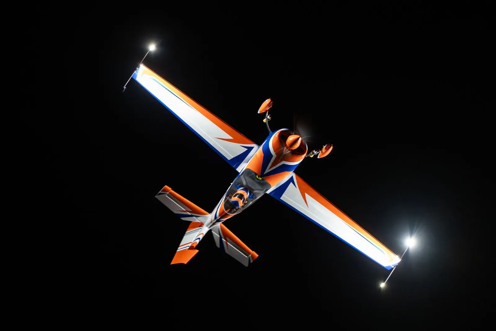Orange-blaues Kunstflugmodell im Nachtflug, die Lucid-Strahler an den Randbögen leuchten